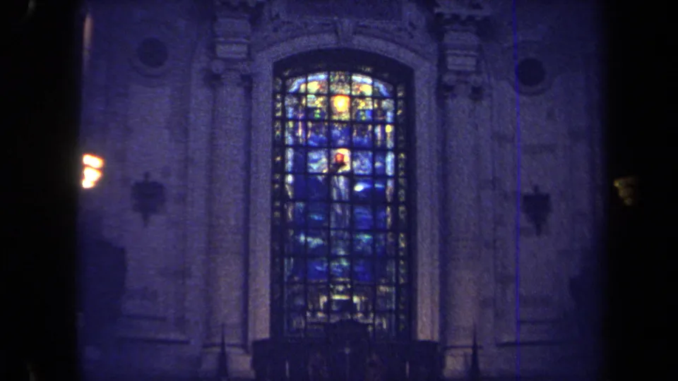 1970 Annapolis 8mm frame centered on a tall stained-glass religious window in carved stone architecture with warm wall sconces.