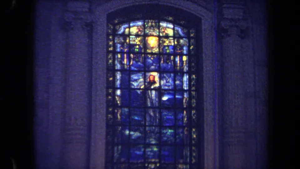 1970 Annapolis 8mm frame showing a closer view of blue stained glass with a robed religious figure and bright yellow glass above.