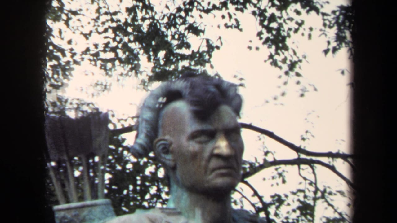 Bronze Native American statue seen close against trees and pale sky.