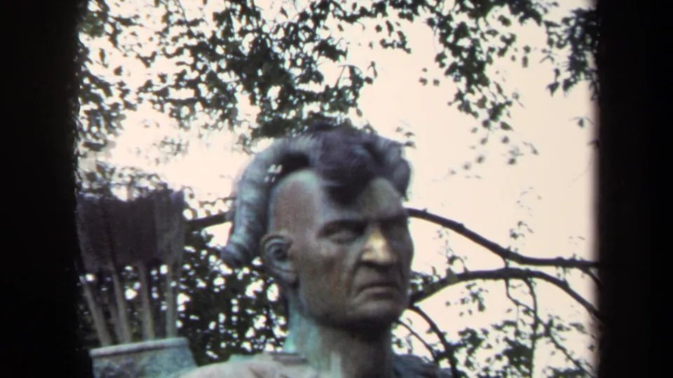 Close 1970 Annapolis 8mm view of a bronze Native American figure with trees and sky behind it.