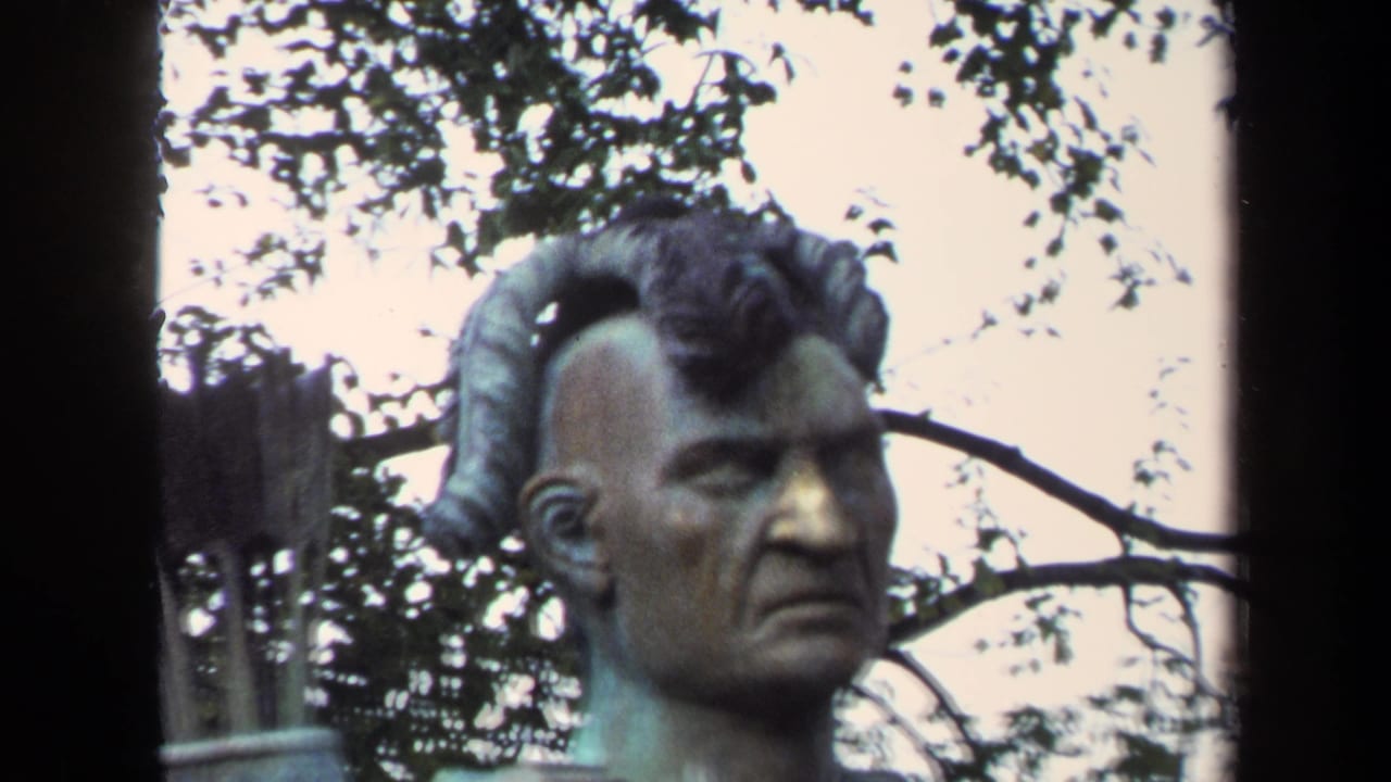 1970 Annapolis home-movie frame showing the statue's head and shoulders against dark tree branches.