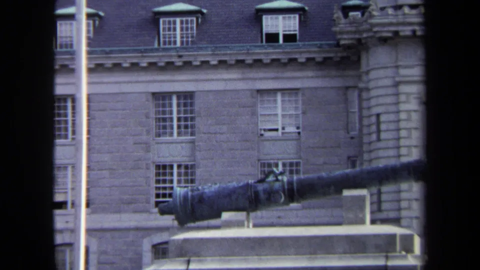 1970 Annapolis 8mm view of a stone institutional building with dormer windows and a mounted cannon in the foreground.
