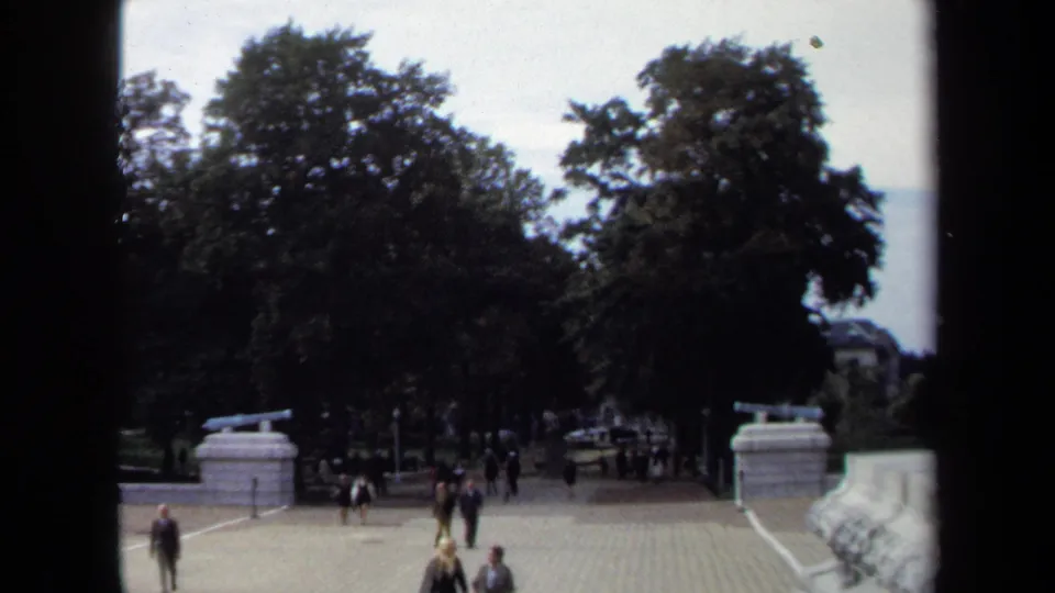 1970 Annapolis wide frame showing visitors walking through a paved tree-lined courtyard, with stone railings and part of the cannon mount at right.