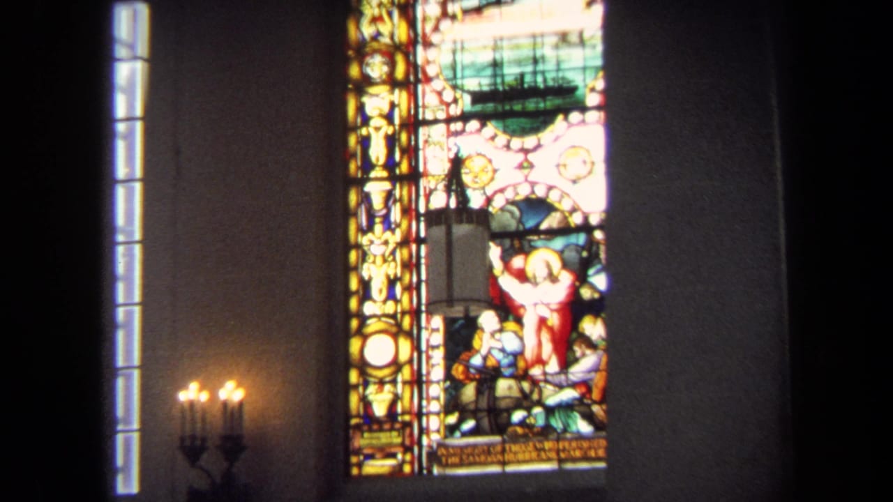 Closer view of a stained glass window with religious figures and a ship motif inside a dim interior.