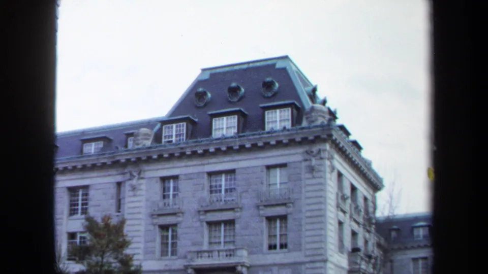 Brief 1970 Annapolis exterior shot of a formal stone building with a mansard roof, dormer windows, and pale cloudy sky.