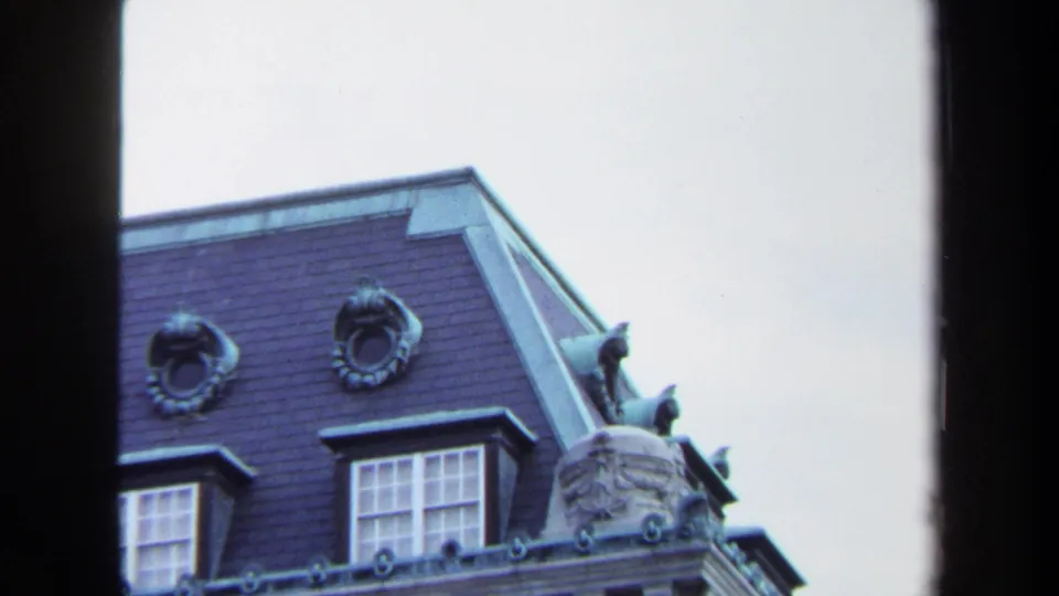 Tight 1970 Annapolis 8mm view of roof medallions, a dormer window, slate-colored mansard surface, and carved stone corner ornament.