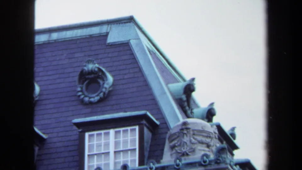 Close 1970 Annapolis frame showing a circular roof ornament, dormer window, sculpted stone corner, finials, and cool-toned 8mm grain.