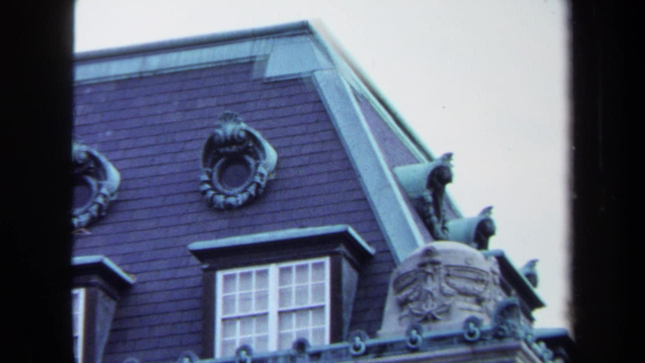 1970 Annapolis home-movie frame showing a slate-roofed stone building with dormer windows and ornate roofline details.