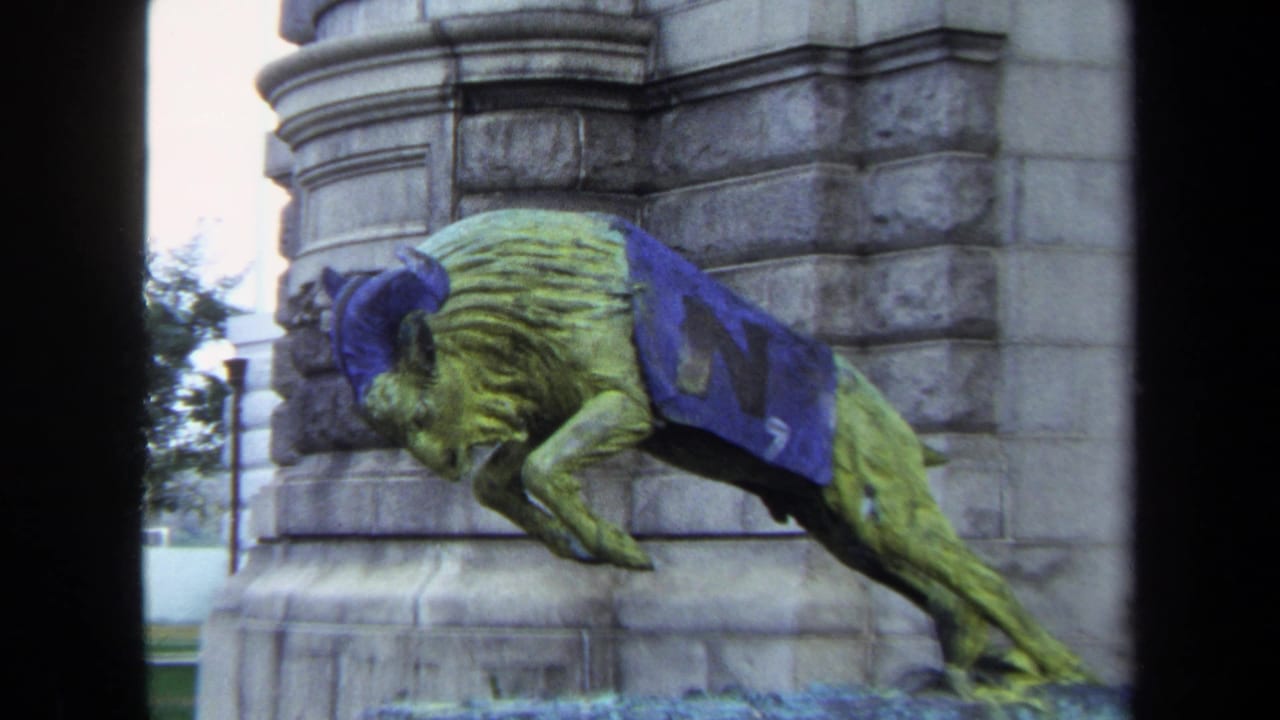 Greenish ram or goat sculpture draped in blue cloth beside stone masonry.