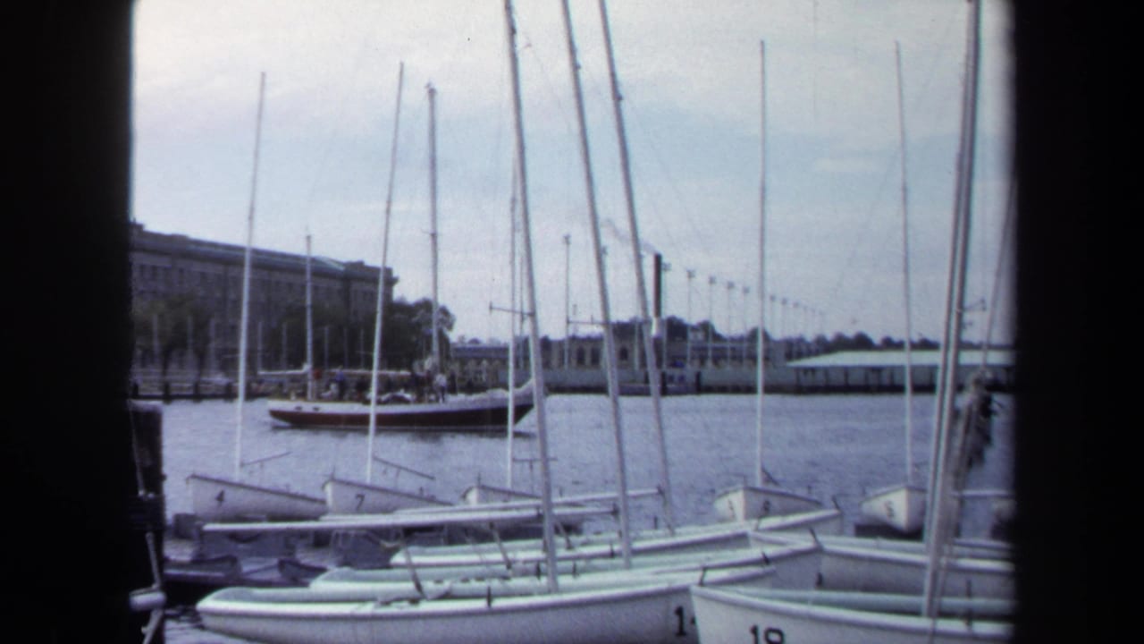 1970 Annapolis harbor view with small numbered sailboats docked in the foreground and low waterfront buildings beyond the water.