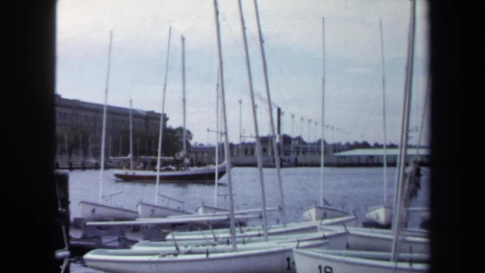 1970 Annapolis harbor view with small numbered sailboats docked in the foreground and low waterfront buildings beyond the water.