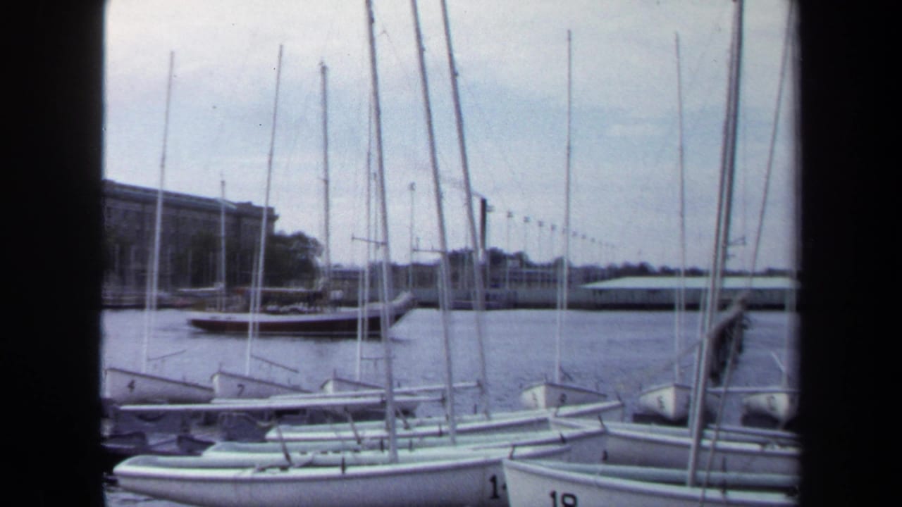 Small sailboats and masts fill the foreground beside calm harbor water.