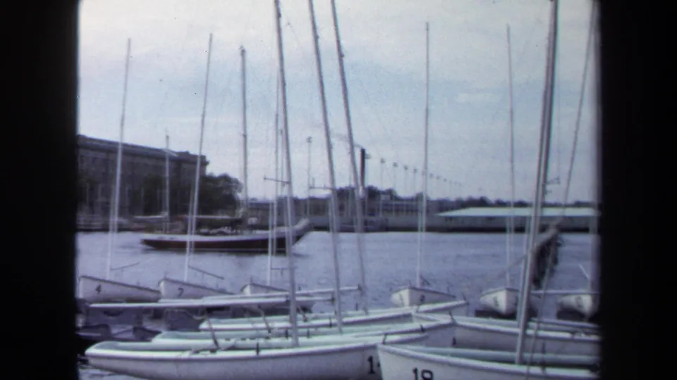 Dockside Annapolis harbor frame from 1970 showing clustered dinghies, vertical masts, a larger sailboat, and distant waterfront structures.