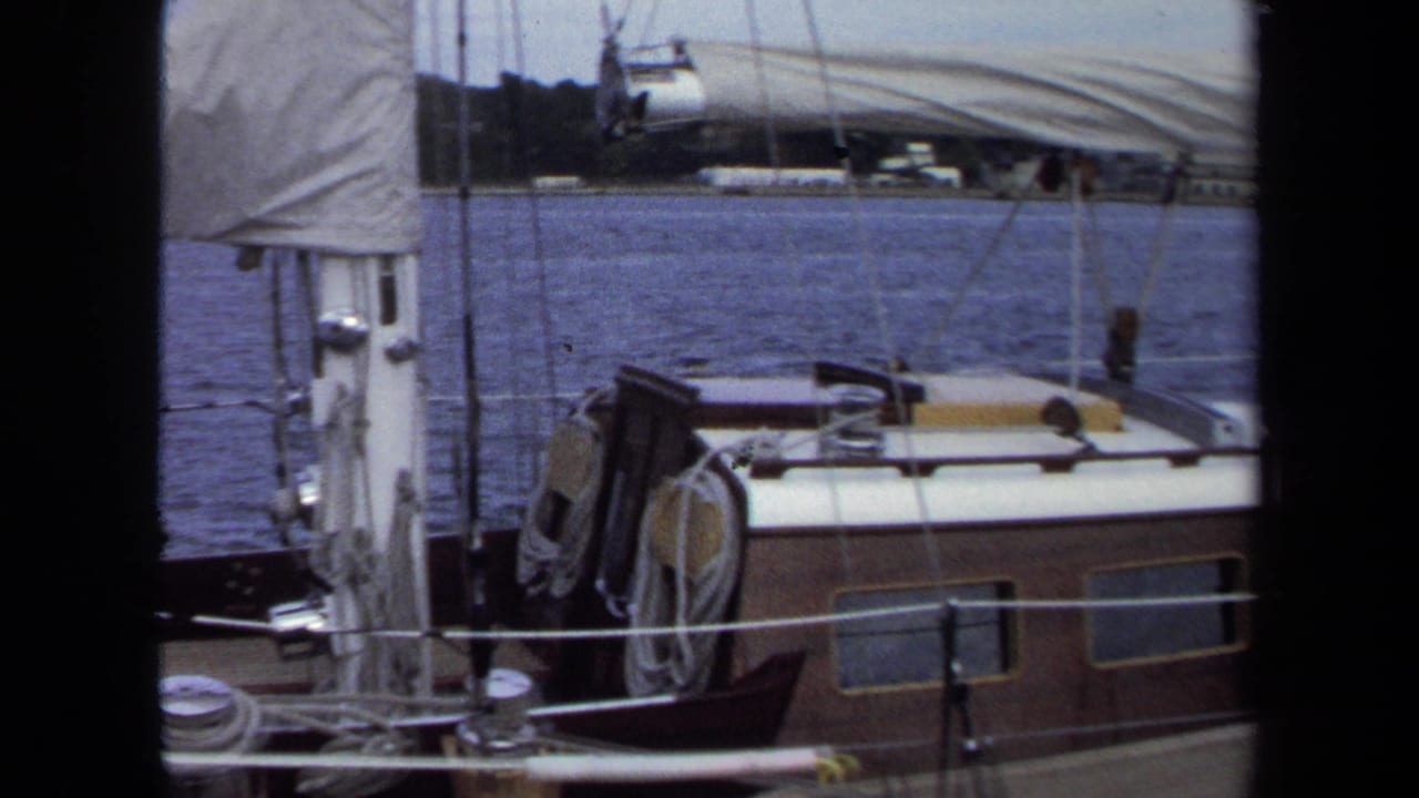 1970 Annapolis home-movie frame with a mast, sail cover, cabin roof, deck lines, and harbor water.