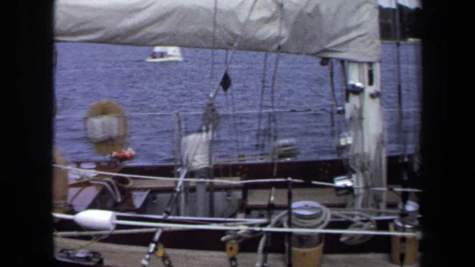 1970 Annapolis frame showing sailboat deck gear, mast lines, railings, blue water, and a small boat in the distance.