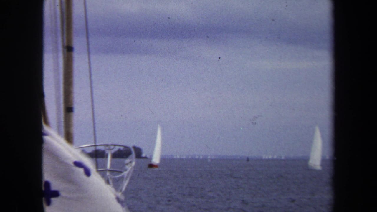 1970 Annapolis 8mm view of white sailboats on calm water, framed by nearby boat rigging and a blue cross-patterned cloth.