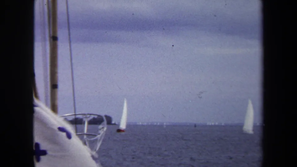 1970 Annapolis 8mm view of white sailboats on calm water, framed by nearby boat rigging and a blue cross-patterned cloth.