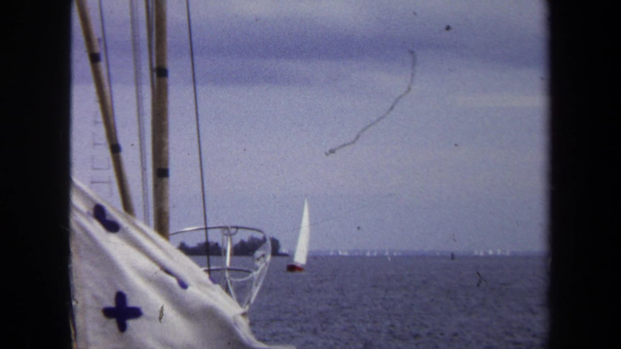 White sailboats on a broad horizon with boat rail and rigging in the foreground.
