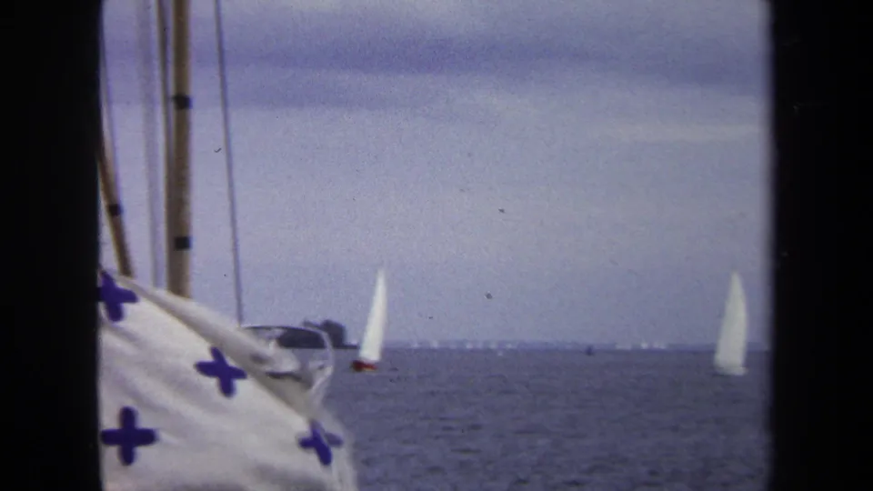 Home-movie frame from Annapolis in 1970 showing nearby boat fabric and rigging with small white sailboats on calm water beyond.