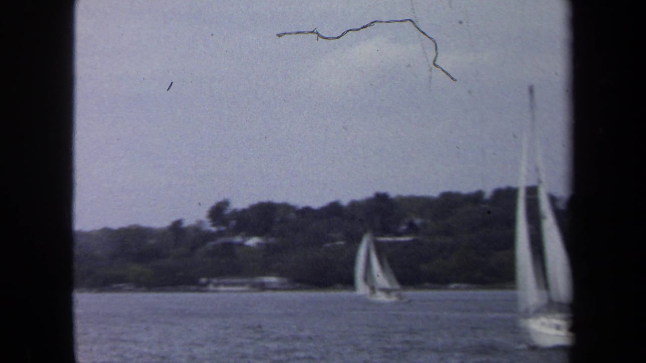 1970 Annapolis-area 8mm frame showing sailboats on calm water with trees and shoreline buildings in the distance.