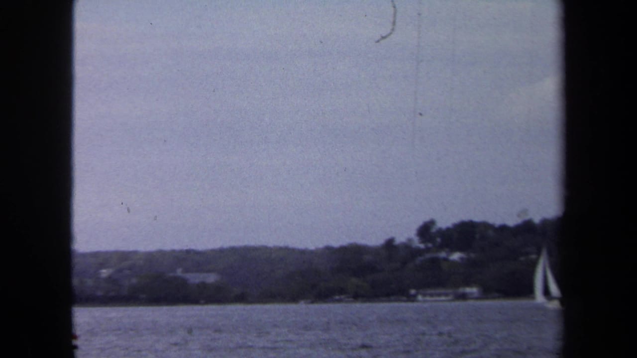 A sailboat passes near the right edge with a wooded shore behind it.
