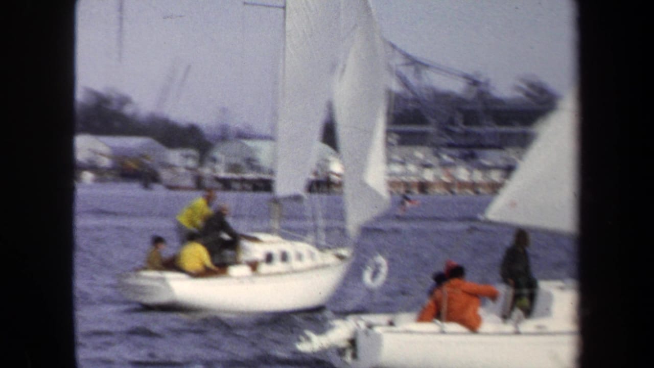 Two sailboats overlap in the frame as crews sit and stand aboard.