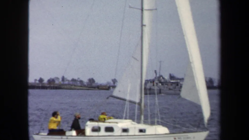 A white sailboat with several people aboard moves through calm water in this soft 8mm Annapolis sailing view.