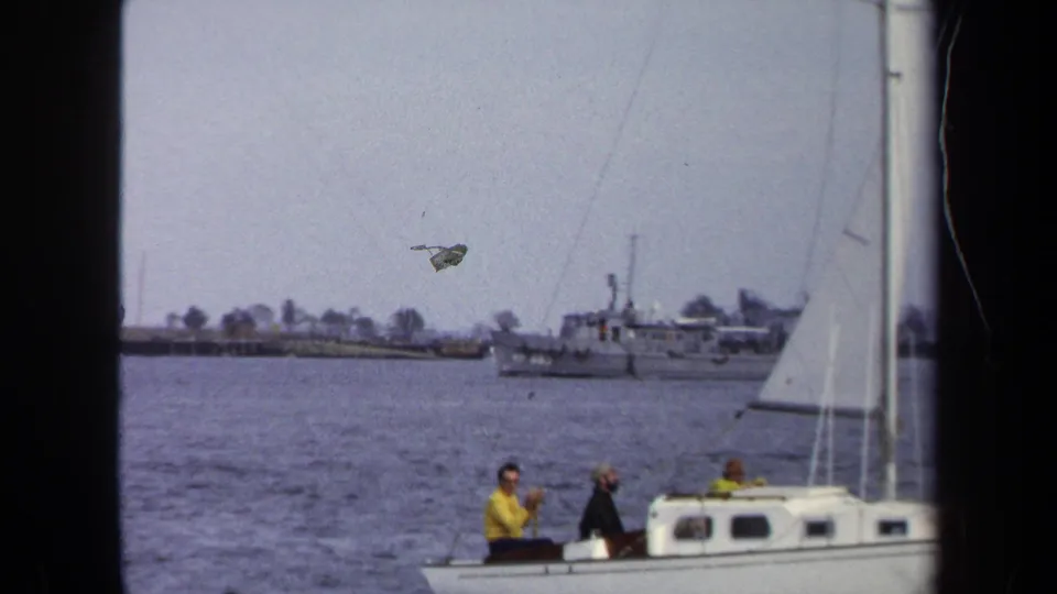 Final frame shows a sailboat crew at right, open water, and a larger distant vessel near the Annapolis shoreline.