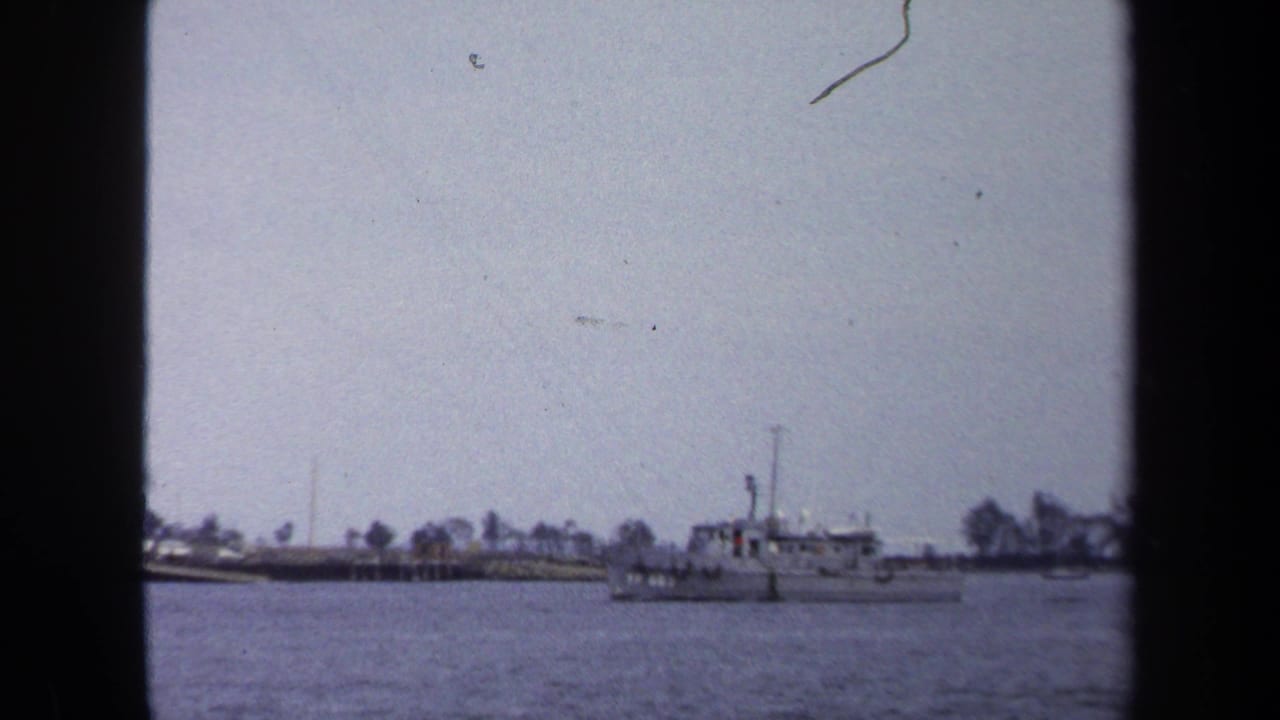 1970 Annapolis waterfront frame with a small motorboat crossing bay water near a low, tree-lined shoreline.