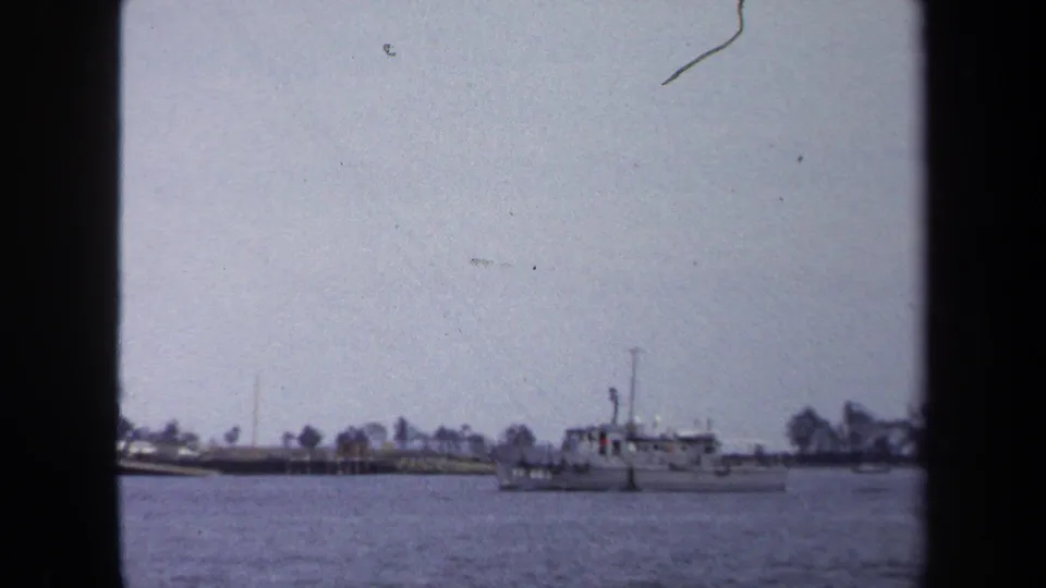 1970 Annapolis waterfront frame with a small motorboat crossing bay water near a low, tree-lined shoreline.