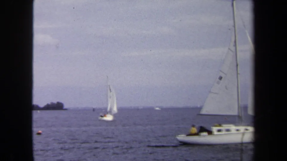 1970 Annapolis boating scene with sailboats on the bay and a larger white sailboat partly entering the foreground.