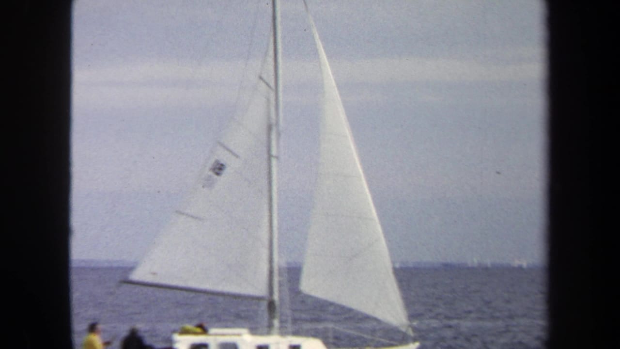 Close sailboat with white sails on open water, partly framed by dark film borders.