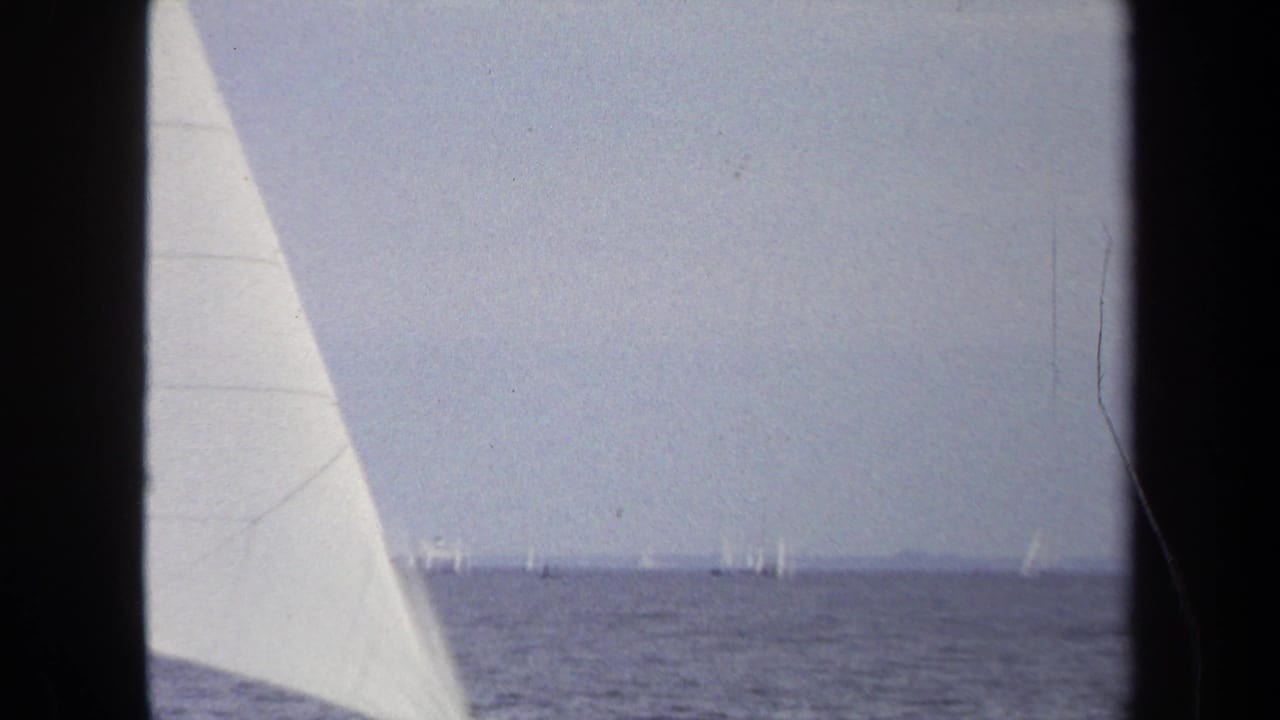 1970 Annapolis sailing footage with a foreground sail, open water, and distant boats scattered near the horizon.