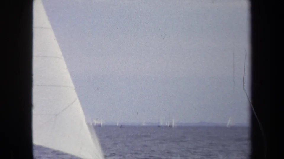 1970 Annapolis sailing footage with a foreground sail, open water, and distant boats scattered near the horizon.