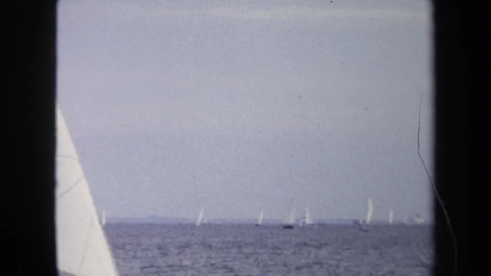 Wide 1970 Annapolis home-movie view with a cropped sail at left and many small sailboats across open water.