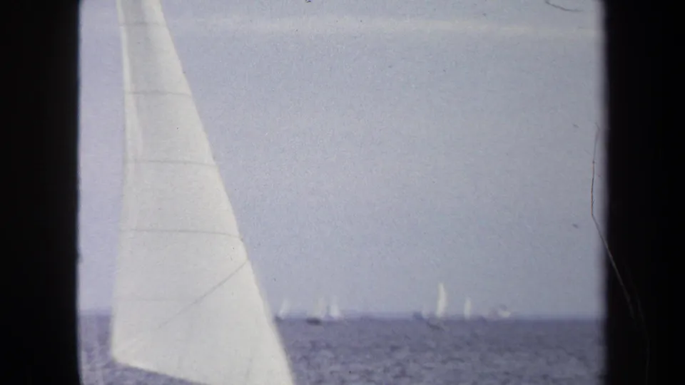 1970 Annapolis frame showing a tall foreground sail and scattered sailboats across the horizon in soft 8mm color.