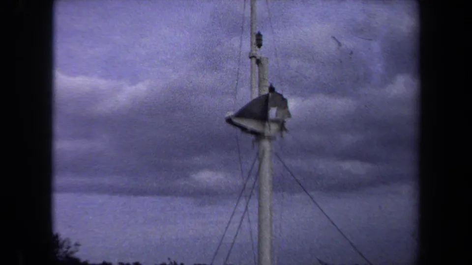 The camera holds on the upper section of a white tower in Annapolis, with a torn flag and support wires silhouetted against dense clouds.
