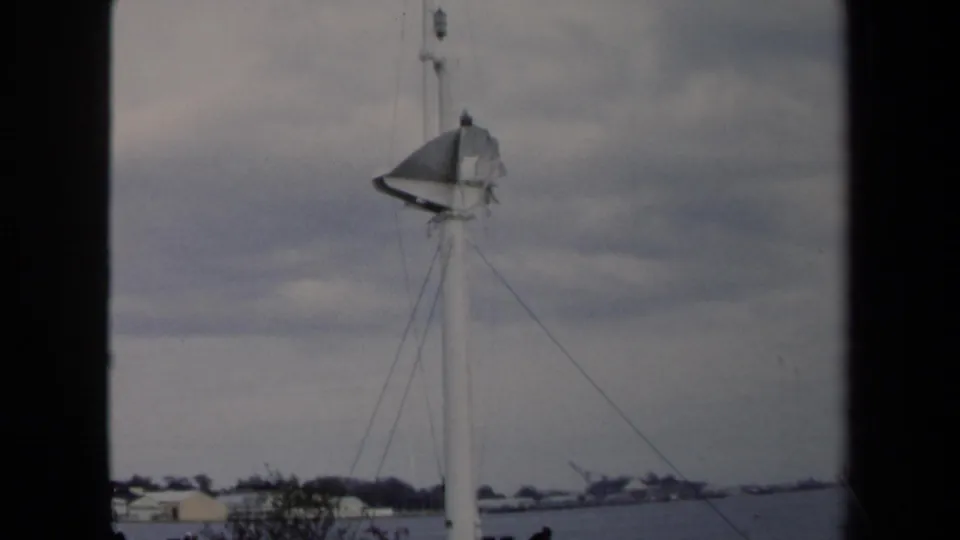1970 Annapolis 8mm frame showing a sailboat mast, rigging lines, cloudy sky, distant shoreline, and dark film-frame edges.