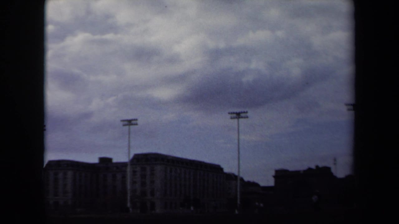 1970 Annapolis home-movie frame showing distant stadium structures and floodlight poles beneath a heavy overcast sky.