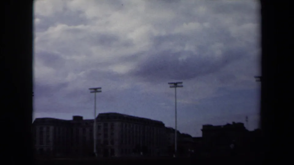 1970 Annapolis home-movie frame showing distant stadium structures and floodlight poles beneath a heavy overcast sky.