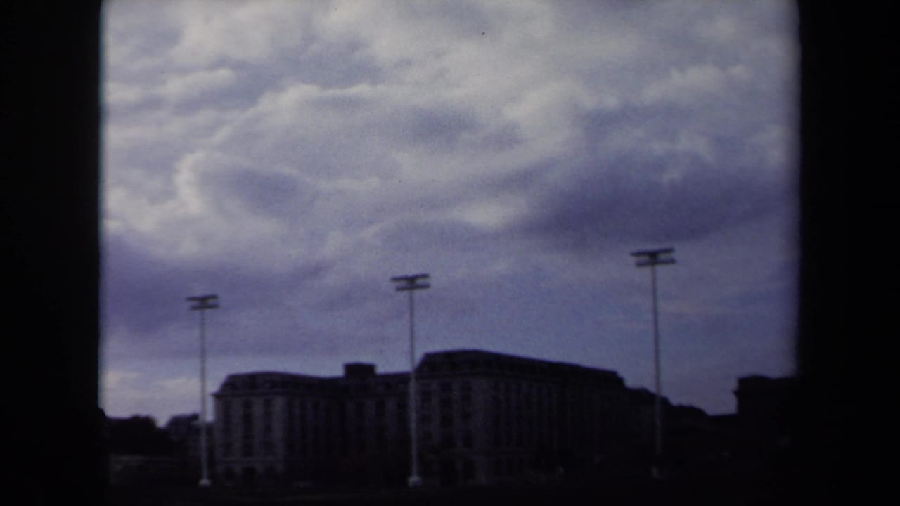 1970 Annapolis frame with tall sports lights and a broad stadium building silhouetted against an overcast daytime sky.