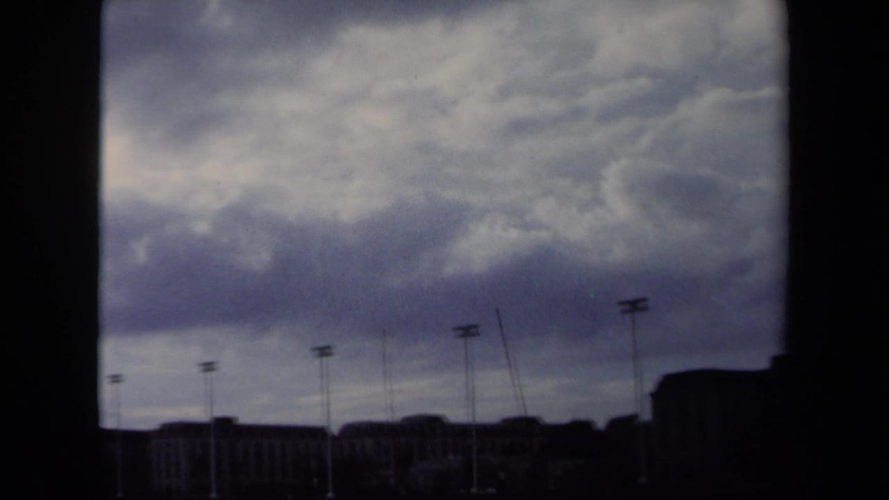 1970 Annapolis waterfront view with heavy clouds, dark building silhouettes, and tall light poles on 8mm film.
