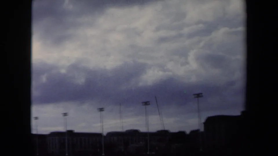 1970 Annapolis waterfront view with heavy clouds, dark building silhouettes, and tall light poles on 8mm film.