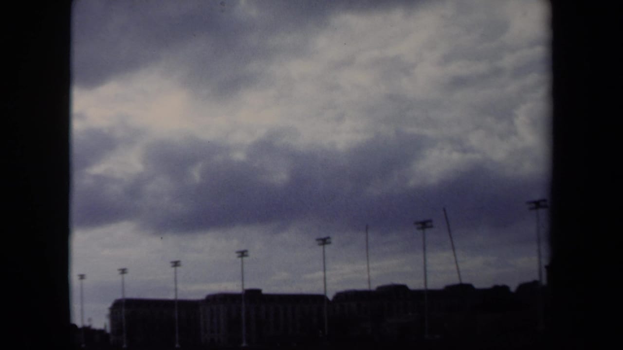 Overcast sky above a dark waterfront skyline with rows of light poles.