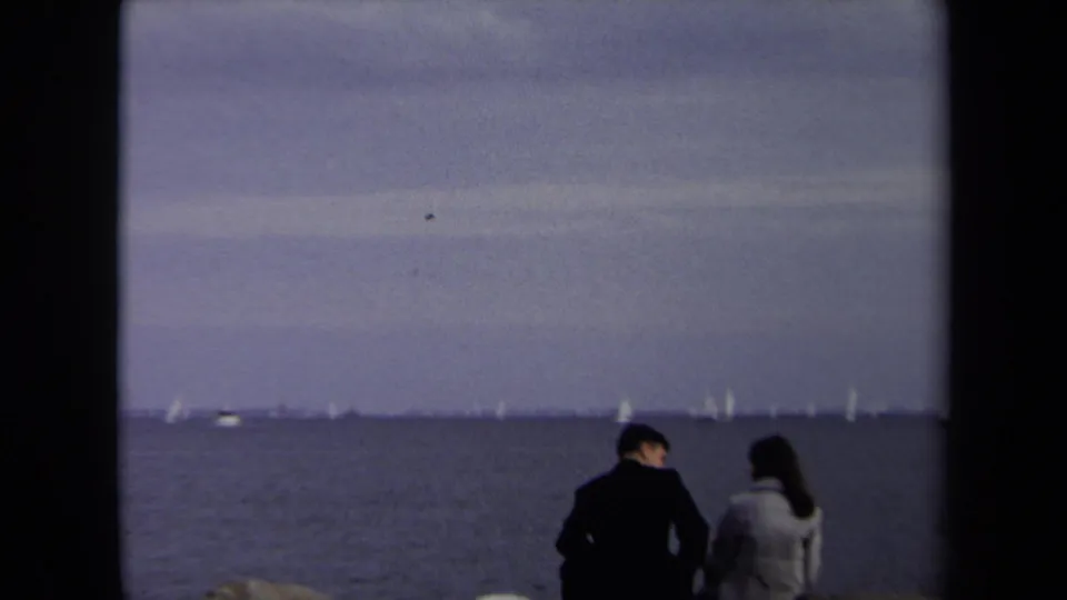 The final frame shows the couple seated close together by the Annapolis waterline, with sailboats visible across the muted horizon.