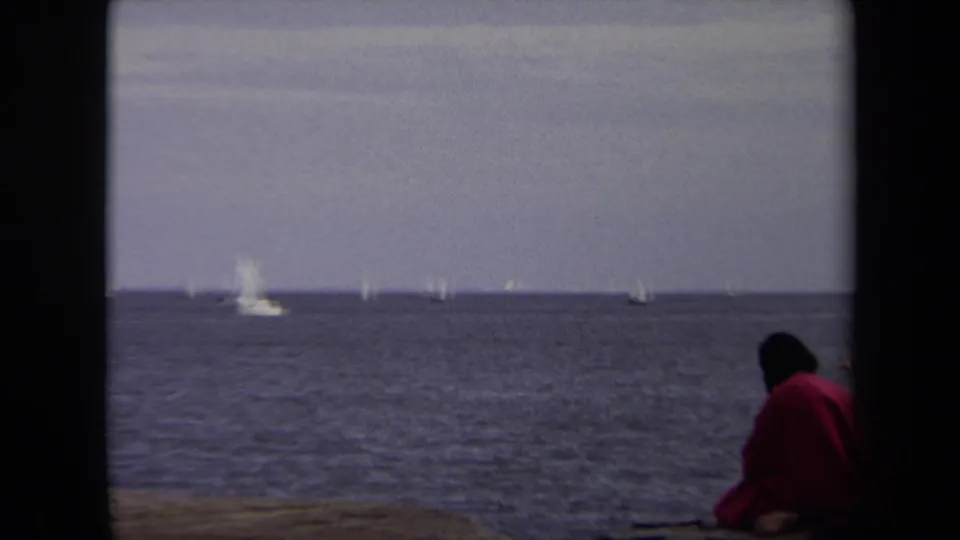 A red-jacketed person sits partly cropped at the right edge of the frame, looking toward distant sailboats on the Annapolis waterfront.