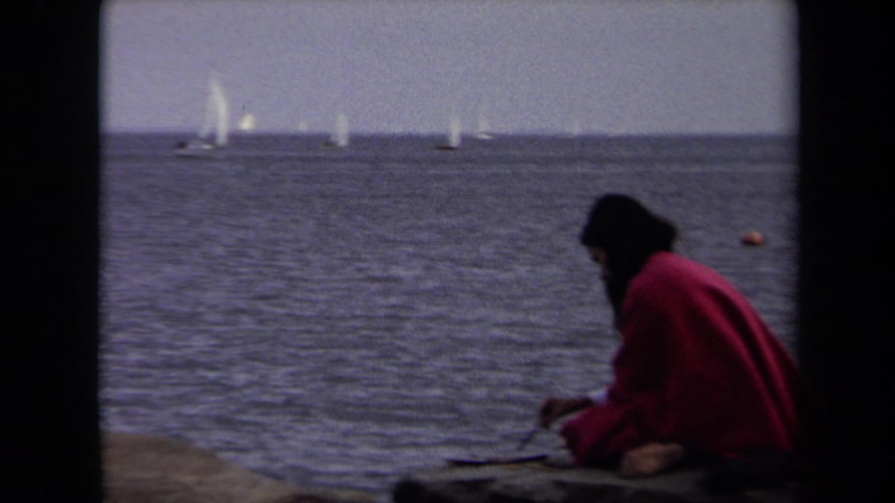 In supported 1970 Annapolis footage, a woman in a red coat sits at the waterfront with sailboats on the horizon.