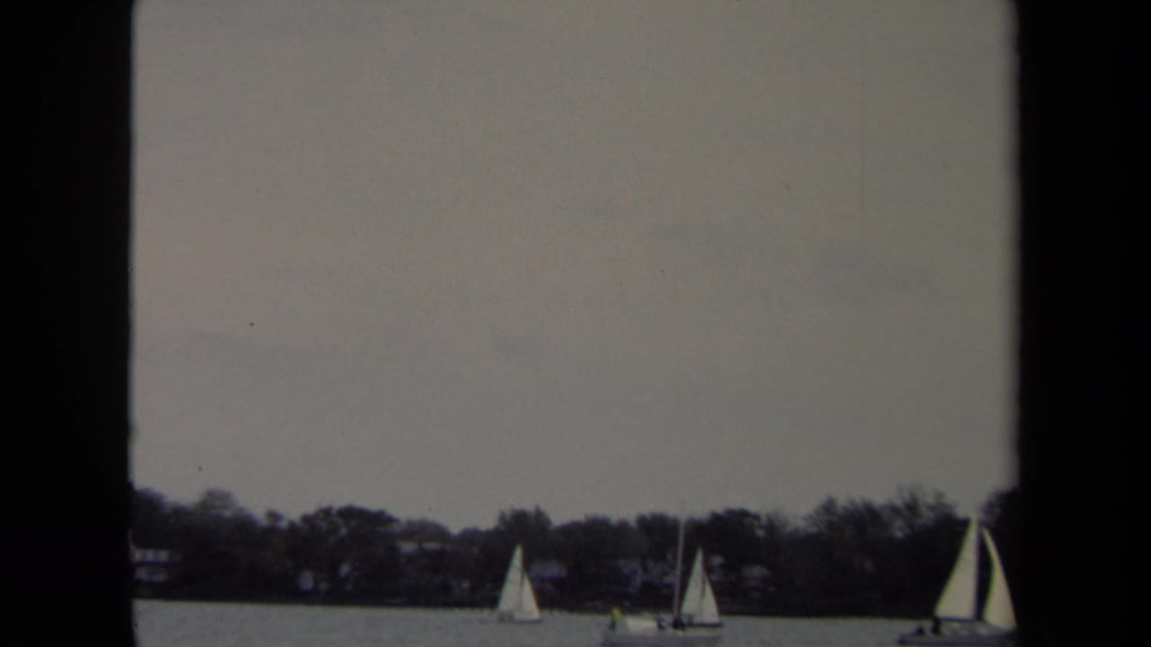 1970 8mm Annapolis home-movie frame showing distant sailboats on calm water under an overcast sky.