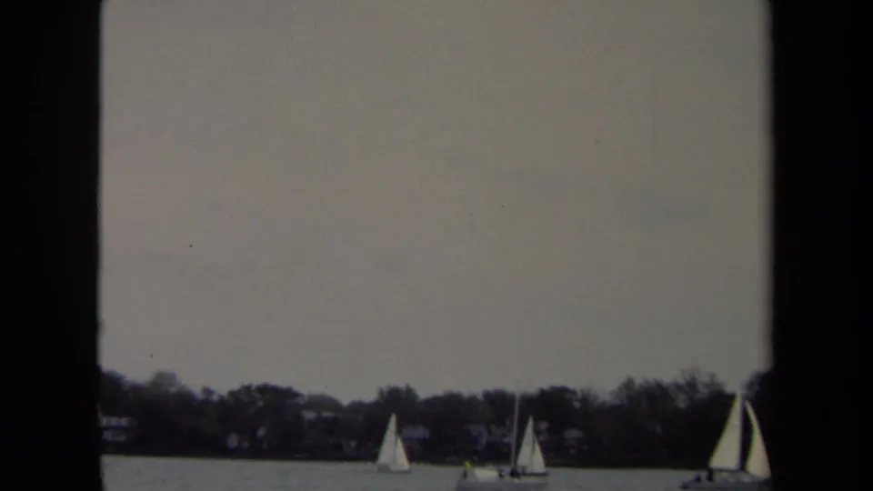 1970 8mm Annapolis home-movie frame showing distant sailboats on calm water under an overcast sky.