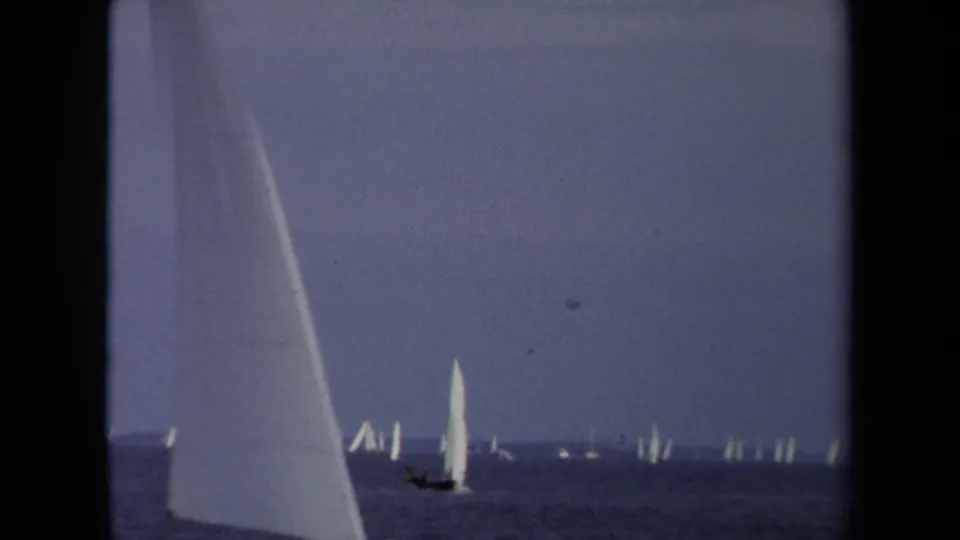 1970 Annapolis sailing scene with a large cropped sail in the foreground and smaller boats across calm blue-gray water.